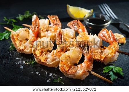 Grilled shrimp skewers served with soy sauce, garlic, fresh parsley and lemon on black plate