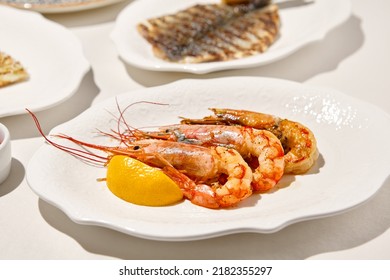 Grilled shrimps on light background with shadows. Grilled prawns with lemon on white table. Aesthetic composition with bbq shrimps. Bbq prawns. Grilled seafood. Summer menu