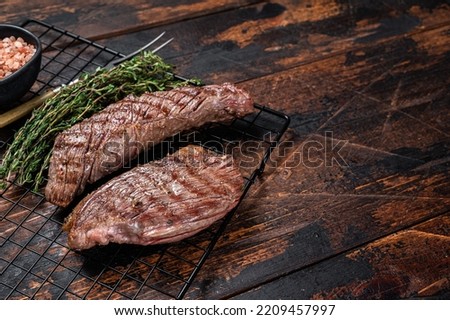 Grilled Sirloin flap or Bavette beef meat steak on a griil with herbs. Wooden background. Top view. Copy space.