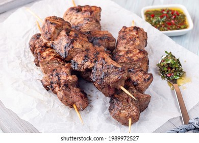 Grilled sirloin tips or beef meat skewers with chimichurri sauce, on a wooden tray, horizontal