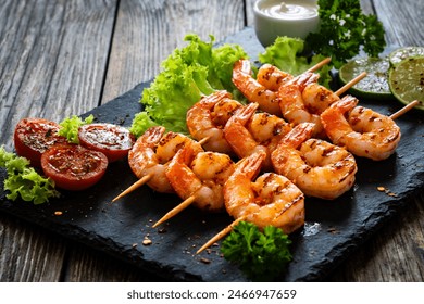 Grilled skewer shrimps and fresh vegetables served on black stony plate on wooden table - Powered by Shutterstock