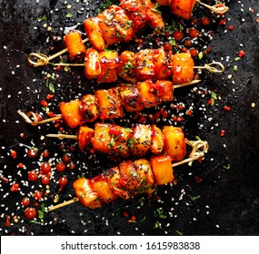 Grilled Skewers With Pineapple Fruit And Chicken Meat  With Sriracha Sauce, Sprinkled With Sesame Seeds, Chilli Pepper And Fresh Herbs On A Black Background, Top View . Fruit And Meat Skewers