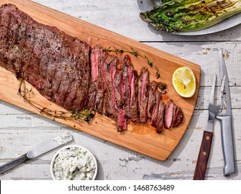Grilled Skirt Steak sliced with Shallot Thyme Butter and asparagus on cutting board with fork and knife