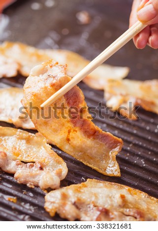 Grilled sliced fresh bacon to crispy by chopsticks and hands on barbecue pan tray in asia family party meal