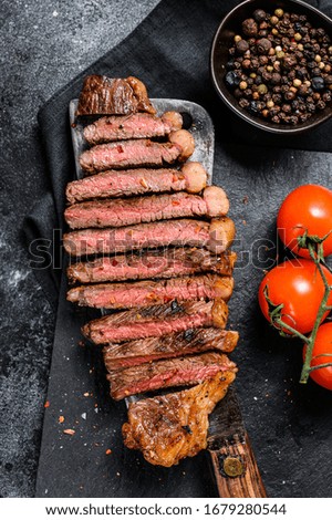 Grilled sliced sirloin steak on a meat cleaver. Black background. Top view
