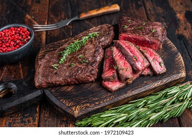 Grilled sliced skirt beef meat steak on a cutting board with herbs. Dark wooden background. Top view