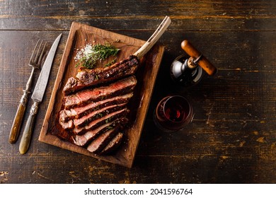 Grilled sliced Tomahawk Steak on bone and glass of Red wine on wooden background