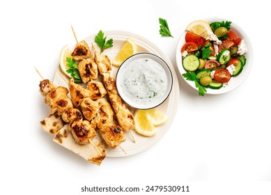 Grilled souvlaki skewers, greek salad and tzatziki sauce on plate isolated on white background, top view. Mediterranean greek lunch with meat kebabs, pita bread and vegetables.