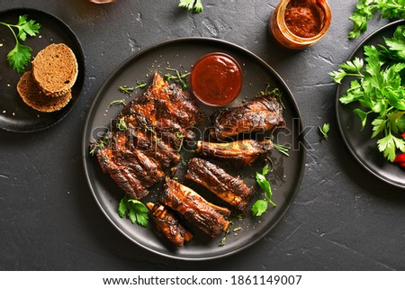 Grilled spare ribs on plate over black stone background. Top view, flat lay