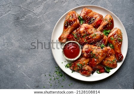 Grilled spicy chicken legs and wings with ketchup on a plate over dark grey slate, stone or concrete background. Top view with copy space.
