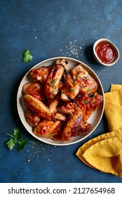 Grilled spicy chicken wings with ketchup on a plate on a dark blue slate, stone or concrete background. Top view with copy space.