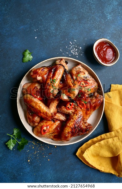 Grilled spicy chicken wings with ketchup on a\
plate on a dark blue slate, stone or concrete background. Top view\
with copy space.