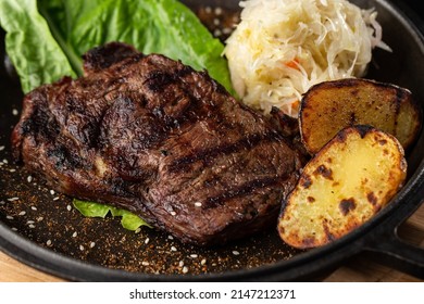 Grilled Steak With Baked Golden Potatoes Served With Sour Cabbage And Red Sauce On A Dark Background. Delicious Recipe. Pork Fillet Cooked On Skillet For Dinner . Fried Juicy Meat Texture.