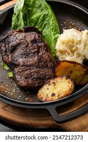 Grilled Steak With Baked Golden Potatoes Served With Sour Cabbage And Red Sauce On A Dark Background. Delicious Recipe. Pork Fillet Cooked On Skillet For Dinner . Fried Juicy Meat Texture.