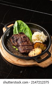 Grilled Steak With Baked Golden Potatoes Served With Sour Cabbage And Red Sauce On A Dark Background. Delicious Recipe. Pork Fillet Cooked On Skillet For Dinner . Fried Juicy Meat Texture.