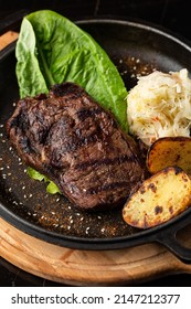 Grilled Steak With Baked Golden Potatoes Served With Sour Cabbage And Red Sauce On A Dark Background. Delicious Recipe. Pork Fillet Cooked On Skillet For Dinner . Fried Juicy Meat Texture.