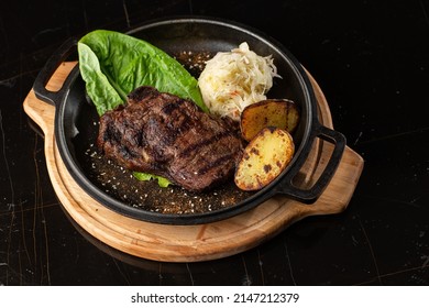 Grilled Steak With Baked Golden Potatoes Served With Sour Cabbage And Red Sauce On A Dark Background. Delicious Recipe. Pork Fillet Cooked On Skillet For Dinner . Fried Juicy Meat Texture.