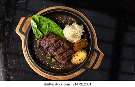 Grilled Steak With Baked Golden Potatoes Served With Sour Cabbage And Red Sauce On A Dark Background. Delicious Recipe. Pork Fillet Cooked On Skillet For Dinner . Fried Juicy Meat Texture.