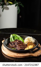 Grilled Steak With Baked Golden Potatoes Served With Sour Cabbage And Red Sauce On A Dark Background. Delicious Recipe. Pork Fillet Cooked On Skillet For Dinner . Fried Juicy Meat Texture.