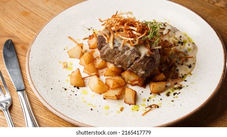 Grilled Steak With Baked Golden Potatoes Served With Crispy Onion On Top On A Brick Background. Delicious Recipe. Pork Fillet Cooked On Skillet For Dinner . Fried Juicy Meat Texture.