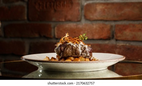 Grilled Steak With Baked Golden Potatoes Served With Crispy Onion On Top On A Brick Background. Delicious Recipe. Pork Fillet Cooked On Skillet For Dinner . Fried Juicy Meat Texture.