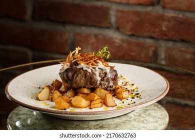 Grilled Steak With Baked Golden Potatoes Served With Crispy Onion On Top On A Brick Background. Delicious Recipe. Pork Fillet Cooked On Skillet For Dinner . Fried Juicy Meat Texture.