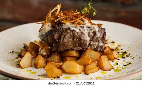 Grilled Steak With Baked Golden Potatoes Served With Crispy Onion On Top On A Brick Background. Delicious Recipe. Pork Fillet Cooked On Skillet For Dinner . Fried Juicy Meat Texture.