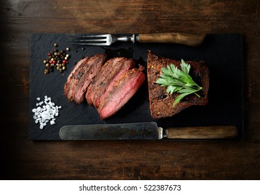grilled steak on a black slate, knife and fork. Top view.