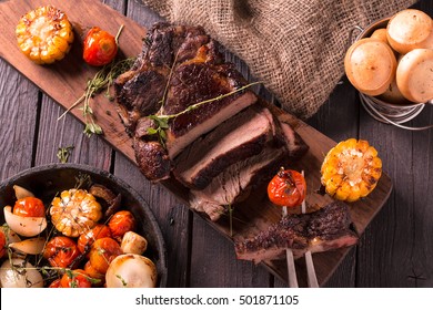 Grilled Steak sliced on a cutting board. Meat with Grilled Vegetables. Wooden background.