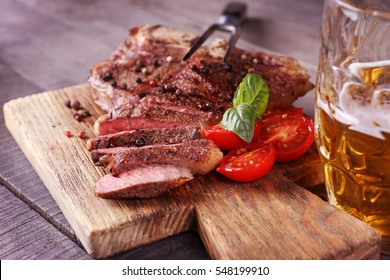 Grilled steak with tomatoes on cutting board and mug of beer, closeup