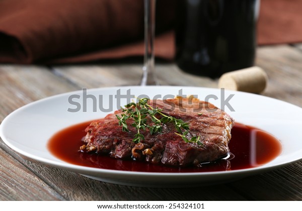 Grilled steak in wine sauce with bottle of\
wine on wooden\
background
