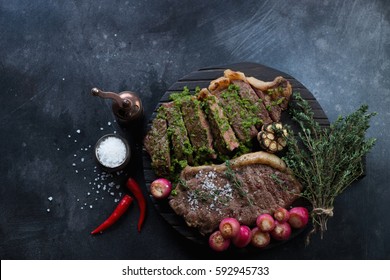 Grilled striploin steaks with fried radish and chimichurri, dark scratched background, top view
