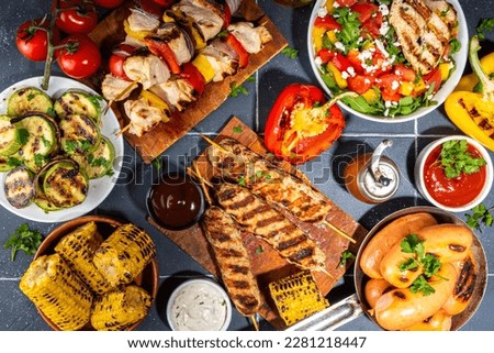 Grilled summer bbq dishes. Bar-b-q party picnic flatlay with various barbecue grill food - shish kebab skewers, grilled corn, salad with bonfire fried chicken, steak, sausages, vegetables top view