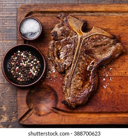 Grilled T-Bone Steak With Salt And Pepper On Cutting Board On Dark Wooden Background