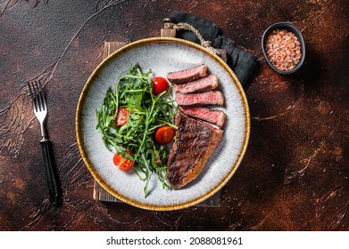 Grilled Top Sirloin Beef Meat Steak In Plate With Vegetable Salad. Dark Background. Top View