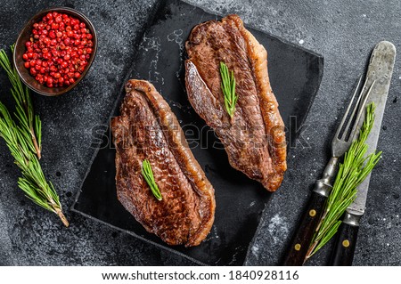 Grilled top sirloin cap or picanha steak on a stone chopping Board. Black background. Top view