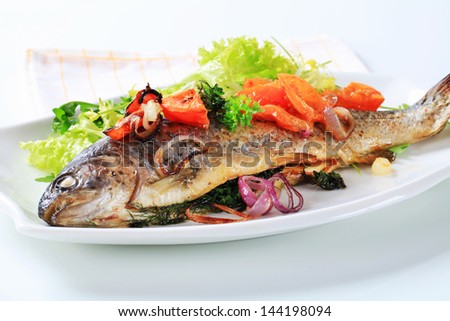 Grilled trout with vegetables and lettuce salad on an oval plate