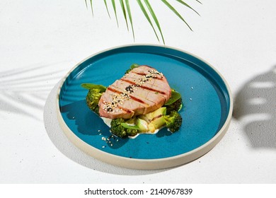 Grilled tuna steak with broccoli and zucchini in modern ceramic plate. Healthy food - roasted tuna with green vegetables. Fish dish in minimal style. Tuna fillet in blue plate with hard shadow - Shutterstock ID 2140967839