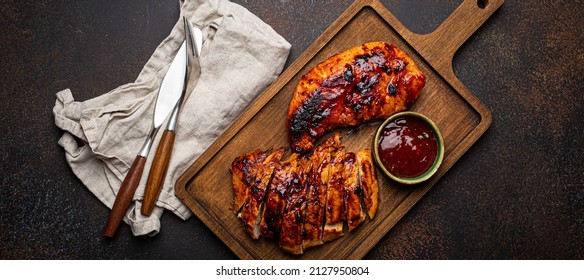 Grilled turkey or chicken marinated fillet with red sauce served and sliced on wooden cutting board on stone brown background from above, poultry breast barbecue 