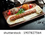 Grilled Turkish adana kebab with grilled vegetables, onion and rice on a wooden board. Dark background.