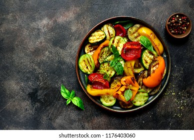 Grilled vegetables (  colorful bell pepper, zucchini, eggplant ) with basil and dry herbs on a plate over dark slate, stone, concrete or metal background.Top view. - Shutterstock ID 1176403060