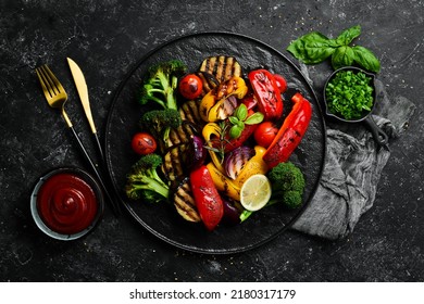 Grilled vegetables (colorful bell pepper, zucchini, eggplant, cherry tomatoes and broccoli) on a black stone plate. Top view. Rustic style. - Shutterstock ID 2180317179