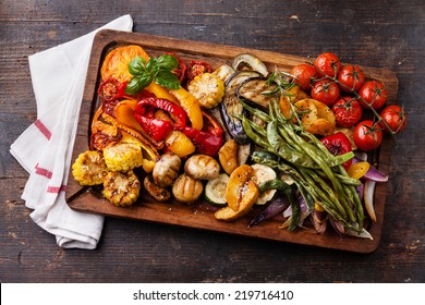 Grilled vegetables on cutting board on dark wooden background