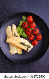 Grilled White Fish Fillet With Baked Tomatoes On The Black Plate