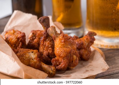 Grilled Wings In The Foreground. Selective Focus On Delicious Chicken Meat Baked Under Bbq Sauce. Wooden Surface And Glasses Of Beer In Background.