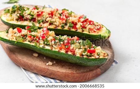 Grilled zucchini stuffed with couscous, tomatoes, cucumber and parsley. Vegan stuffed zucchini on a cutting board. Vegetarian food.