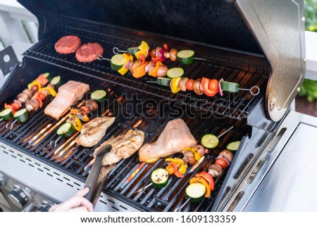 Grilling an Atlantic salmon, chicken breast, vegetable skewers, and vegetarian burgers on an outdoor grill.