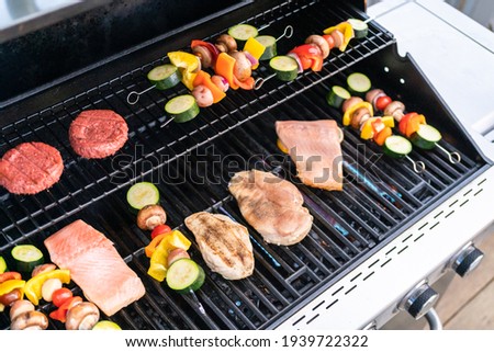 Grilling an Atlantic salmon, chicken breast, vegetable skewers, and vegetarian burgers on an outdoor grill.