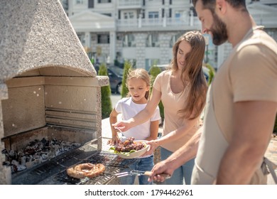 Grilling. Dad Grilling Meat While His Daughter And Wife Watching