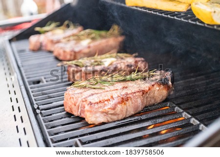 Grilling New York steak with a slice of butter and rosemary on an outdoor gas grill.